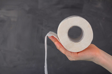 a roll of toilet paper lies on a woman's palm on a gray background