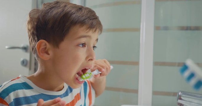 Adorable boy in pyjamas brushing his teeth looking in the bathroom mirror. Close-up side shot.