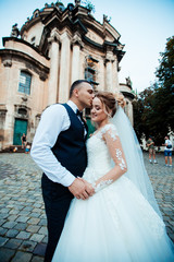 Naklejka premium The bride and groom walk together in the park. Charming bride in a white dress, the groom is dressed in a dark elegant suit.
