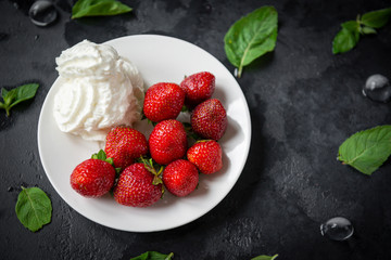 strawberries with cream on a plate, mint leaves on a black background, fresh berries, dessert