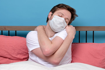 Mature caucasian man in medical mask hugging himself at bed alone.