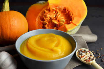Pumpkin soup in a bowl with fresh pumpkins, garlic, croutons and spices on grunge black background with linen cloth