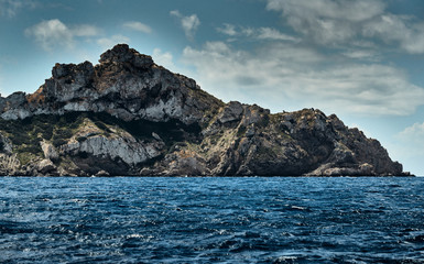 Fototapeta na wymiar The Landscape of the balearic sea and improbable mountains, azure water, the storm sky, lonely buildings at tops of mountains, sail boat is on background