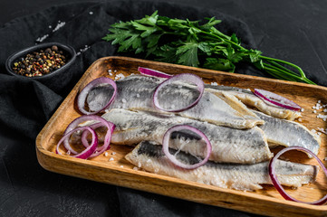 Fillet of salted herring with parsley and red onion. On black rustic background.  Top view. Space for text