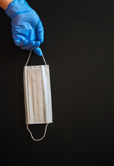 Hand in a transparent glove with a disposable medical mask on a black background. Concept: means of...