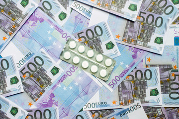 White tablets in a blister lying on a pile of 500 Euro banknotes close-up. Concept: the pharmaceutical business.