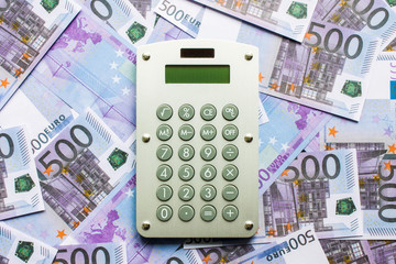Calculator on a scattering of 500 Euro banknotes close-up flat lay.