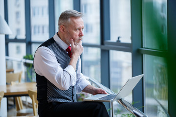 Adult male businessman, teacher, mentor working on a new project. Sits by a large window on the...