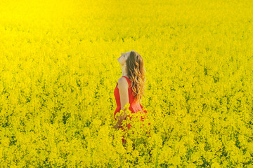 Fototapeta premium Young beautiful girl in a red dress close up in the middle of the yellow field with the radish flowers closeup