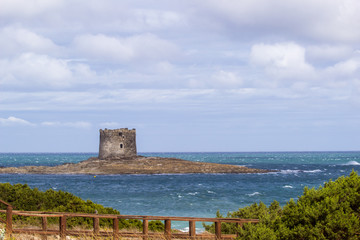 Summer view on the old aragonese tower in La Pelosa Beach.  Beautifull waves with foam, geen trees in Stintino, Sardinia, Italy