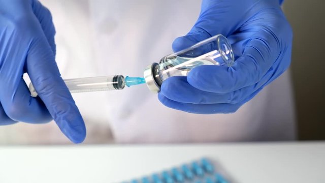 Doctor or nurse in blue gloves filling the syringe with vaccine for injection close up, vaccination and immunisation concept.