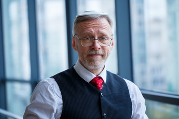 Smiling happy managing director thinks about his successful career development while stands in his office near the background of a window with copy space