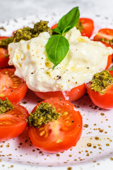 Italian cheese stracciatella (burrata) on small plate served with fresh tomatoes and basil. Gray background. Space for text.