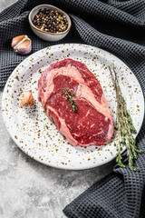 Raw fresh meat Ribeye Steak with seasoning on cutting board. Rib eye beef steak. gray background. top view