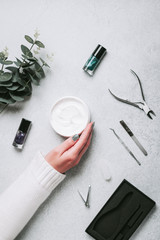 Woman hands, nail polish, manicure tools and hand cream on grey concrete table top flat lay. How to do manicure at home concept. Do manicure by yourself while staying at home, top view
