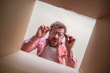 Strange man looks at the bottom of an unpacked delivered box with a parcel with a disappointed...