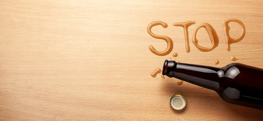 Beer bottle and spilled beer in the shape of the word STOP. Ban alcohol