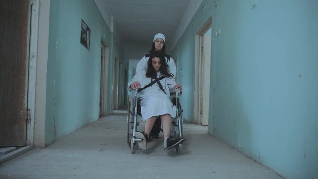 Female Nurse Pushing Patient In The Wheelchair Through The Hospital Corridor