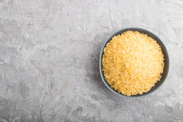 Blue ceramic bowl with raw golden rice on a gray concrete background. Top view, copy space.