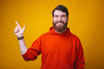 Portrait of a young smiling man pointing at his right yellow background where there is space for your text.