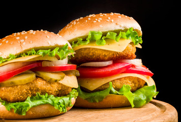 .two burgers on a wooden board on a black background.