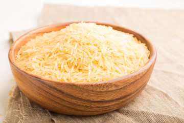 Wooden bowl with raw golden rice and wooden spoon on a white wooden background. Side view, selective focus.