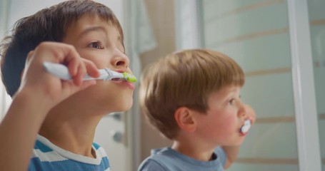 Kids in pyjamas brushing their teeth infront of the bathroom mirror. Close-up side shot.