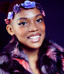 young pretty african american woman in spotted fur coat and flowers on head smiling on black background, fashion people concept