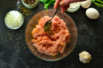 Cooking process. Minced meat and ingredients, salt, pepper, spices, onions, eggs, parsley, mix the ingredients with a spoon. A woman is preparing minced chicken for meatballs. Top view.