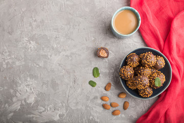 Chocolate caramel ball candies with almonds and a cup of coffee on a gray concrete background and red textile. top view, copy space.