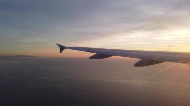 Wing side view of a plane flying over the Pacific Ocean at sunset
