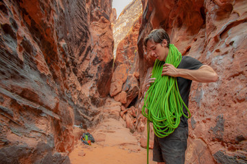 Male rock climber in Nevada desert canyon gathers green rope