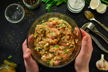 Cooking process. Minced meat and ingredients, salt, pepper, spices, onions, eggs, parsley, mix the ingredients with a spoon. A woman is preparing minced chicken for meatballs. Top view.