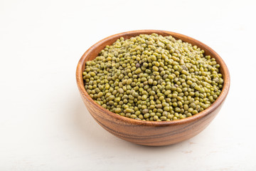 Wooden bowl with raw green mung bean on a white wooden background. Side view.