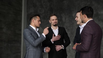 Four friendly male ceo coworkers say goodbye indoors. Fun real conversation of men staff in suit enjoying good lol joke together in office room. Handshake, hug of interacting talking humorous joy team