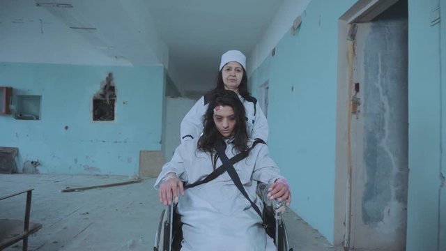 Female Nurse Pushing Patient In The Wheelchair Through The Hospital Corridor