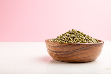 Wooden bowl with raw green mung bean on a white and pink background. Side view, copy space.