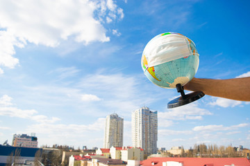 Earth globe in a protective mask in a man’s hand against the background of blue sky and cityscape