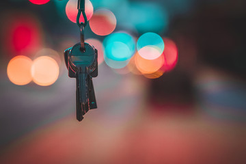 A set of modern metal keys hanging from above with a blurred background of red and blue lights....