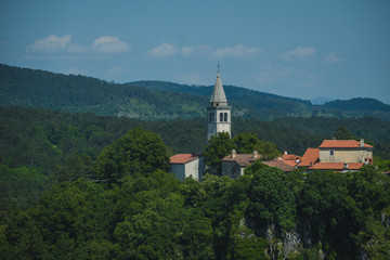 Fototapeta na wymiar Village of Skocjan, with a visible bell tower of St. Kancijan church, rising way above the Skocjan Caves gorge on a summer day.