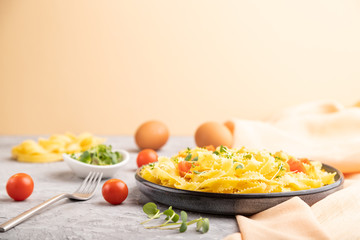 Reginelle semolina pasta with tomato, eggs and microgreen sprouts on a gray and orange background. Side view, selective focus.