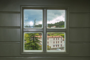 Panorama of the city of Stanjel in Slovenia on a cloudy spring day, looking through window with a wooden cross on it.