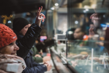 Obraz na płótnie Canvas Person ordering a fresh kebab or gyros in a fast food stall or vendor outside in a city. Visible hands showing V sign to order food over the counter in festive evening.