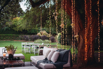 Decoracion de jardin con luces, plantas y sillones de madera.