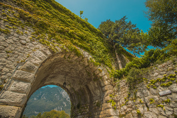 Fototapeta na wymiar Stone arch made to enter the city through the city walls of medieval town of Venzone in northern Italy. Beautiful arch covered in green foliage