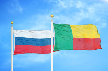 Russia and Benin  two flags on flagpoles and blue cloudy sky
