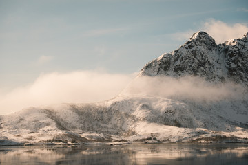 peaks of norway in black and white. peaks near to svolvaer town in lofoten islands during winter. snowy mountains shows their peaks partly hidden by clouds. cottage next to lake and moutains.ambient