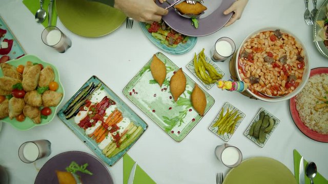 Top view of a traditional delicious Turkish family dinner table. Pickles, chicken rice, haricot beans cooked with tomato, kibbeh, pastry, fried vegetables and green beans. Family serving themselves.