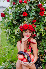 Attractive girl with a wreath of red roses with a basket of vegetables: tomatoes, eggplants, peppers.