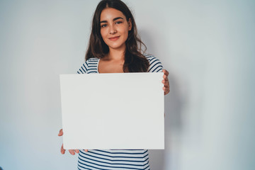 Portrait of young attractive woman holding blank paper against white background, hipster girl...